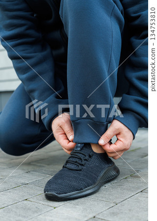 A person is tying the shoelaces on their stylish and modern athletic sneakers while they are dressed in comfortable activewear that is perfect for various types of physical activities and exercises 134753810