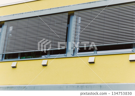 The innovative and modern design of architectural windows incorporates elegant blinds and showcases a vibrant yellow facade, creating a striking appearance that enhances urban aesthetics The innovative and modern design of architectural windows incorporates elegant blinds and showcases a vibrant yellow facade, creating a striking appearance that enhances urban aesthetics 134753830