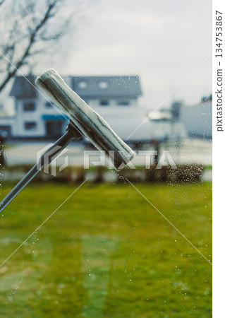 Using a squeegee to clean a window leads to a clear and bright outdoor view, making it perfect for visuals related to home cleaning and maintenance tasks that showcase cleanliness and hygiene Using a squeegee to clean a window leads to a clear and bright outdoor view, making it perfect for visuals related to home cleaning and maintenance tasks that showcase cleanliness and hygiene 134753867