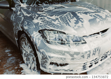 A shiny silver car is getting a thorough soap foam wash in a clean and wellmaintained service area, ensuring that it stays in topnotch condition and maintains its brilliant shine 134753872