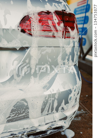 A shiny silver car, thoroughly covered in foam, is undergoing a meticulous cleaning process at an automatic car wash to achieve impeccable cleanliness and a polished appearance that truly stands out 134753877