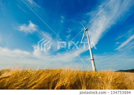 A majestic wind turbine tower stands tall against a backdrop of a crystal clear blue sky, surrounded by vast and expansive golden wheat fields, creating a breathtakingly beautiful landscape A majestic wind turbine tower stands tall against a backdrop of a crystal clear blue sky, surrounded by vast and expansive golden wheat fields, creating a breathtakingly beautiful landscape 134753894