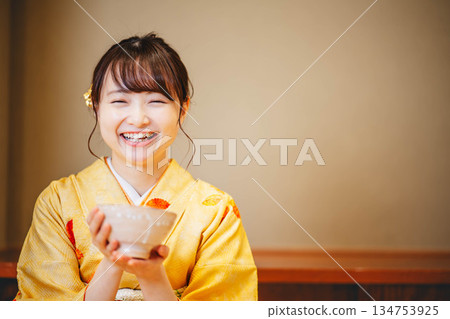 一位身著和服的年輕女子正在用碗喝茶。 134753925