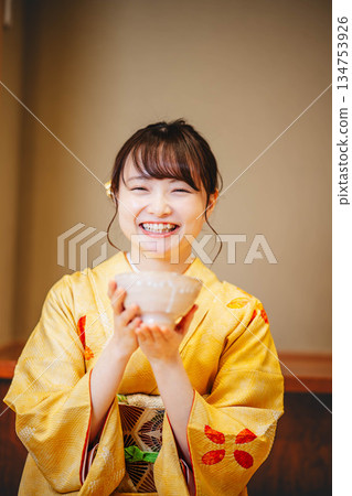 一位身著和服的年輕女子正在用碗喝茶。 134753926