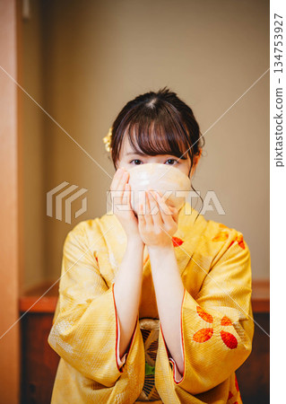 一位身著和服的年輕女子正在用碗喝茶。 134753927