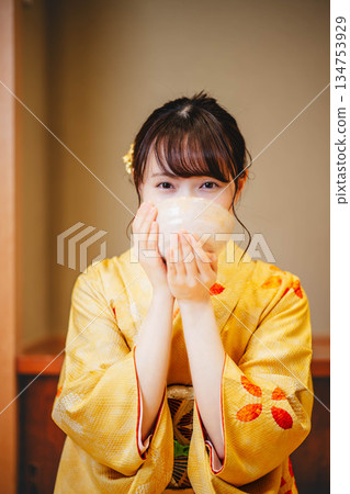 一位身著和服的年輕女子正在用碗喝茶。 一位身著和服的年輕女子正在用碗喝茶。 134753929