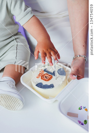 A joyful toddler having fun while enjoying some delicious cake with adult supervision nearby A joyful toddler having fun while enjoying some delicious cake with adult supervision nearby 134754059