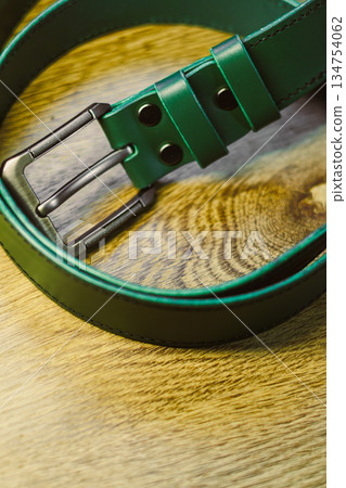This fashionable and stylish green leather belt, featuring a sleek and elegant metal buckle, beautifully enhances both casual and formal outfits, and is artfully displayed on a rich wooden surface This fashionable and stylish green leather belt, featuring a sleek and elegant metal buckle, beautifully enhances both casual and formal outfits, and is artfully displayed on a rich wooden surface 134754062