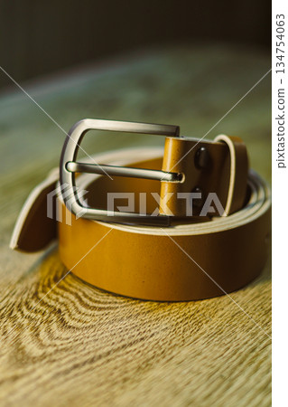 An Elegant Brown Leather Belt featuring a Silver Buckle beautifully displayed on a rustic Wooden Background, making it the perfect accessory to enhance any stylish outfit you choose to wear An Elegant Brown Leather Belt featuring a Silver Buckle beautifully displayed on a rustic Wooden Background, making it the perfect accessory to enhance any stylish outfit you choose to wear 134754063