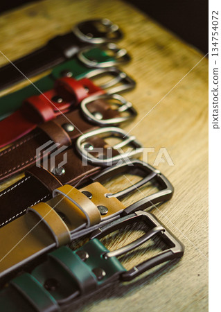 A stunning collection of vibrant and colorful leather belts is beautifully displayed on a rustic wooden surface, highlighting their unique styles and fashionforward designs for all to admire 134754072