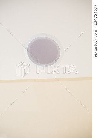 A white circular air vent is currently hanging from the ceiling of a room 134754077