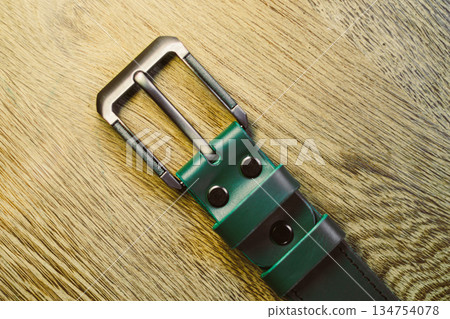 This sophisticated stylish green and gray leather belt features a sleek metal buckle and is beautifully displayed on a rustic wooden surface, highlighting its fashionable design and trendy appeal This sophisticated stylish green and gray leather belt features a sleek metal buckle and is beautifully displayed on a rustic wooden surface, highlighting its fashionable design and trendy appeal 134754078