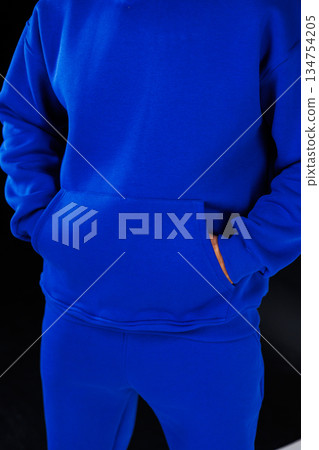 A person in a blue hoodie and pants with hands in pockets A person in a blue hoodie and pants with hands in pockets 134754205
