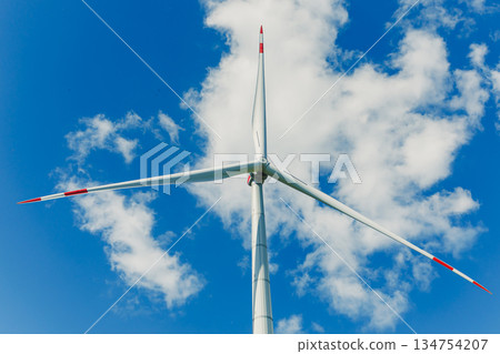 A tall wind turbine stands against a vibrant blue sky with fluffy white clouds, symbolizing the importance of renewable energy in promoting sustainability and supporting ecological health 134754207