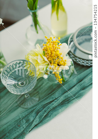 A vibrant floral arrangement in elegant glass vases on a white table with soft green fabric underneath creates a serene atmosphere that fosters relaxation and appreciation of natures beauty 134754215