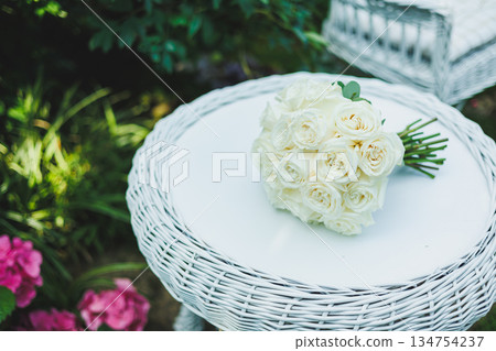 An Elegant White Rose Bouquet Arranged on a Wicker Table Set Within a Beautiful Garden Setting An Elegant White Rose Bouquet Arranged on a Wicker Table Set Within a Beautiful Garden Setting 134754237