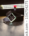 This is a stylish black leather belt featuring a shiny buckle, elegantly displayed on a wooden surface under gentle, soft lighting, showcasing its aesthetic appeal and refined design 134754275