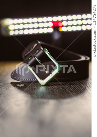 This is a stylish black leather belt featuring a shiny buckle, elegantly displayed on a wooden surface under gentle, soft lighting, showcasing its aesthetic appeal and refined design This is a stylish black leather belt featuring a shiny buckle, elegantly displayed on a wooden surface under gentle, soft lighting, showcasing its aesthetic appeal and refined design 134754275