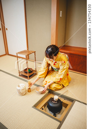 一位年輕貌美的和服女子正在日式房間裡進行茶道表演。 一位年輕貌美的和服女子正在日式房間裡進行茶道表演。 134754330