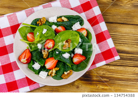 Fresh healthy salad with strawberry, spinach, walnuts and feta cheese on wooden table. Top view 134754388