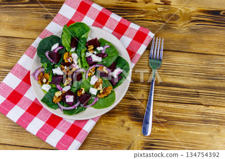 Tasty spinach salad with boiled beetroot, feta cheese, walnut and red onion on wooden table. Top view. Healthy vegetarian food Tasty spinach salad with boiled beetroot, feta cheese, walnut and red onion on wooden table. Top view. Healthy vegetarian food 134754392