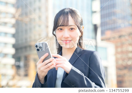 A woman in a suit using a smartphone in an office district 134755299