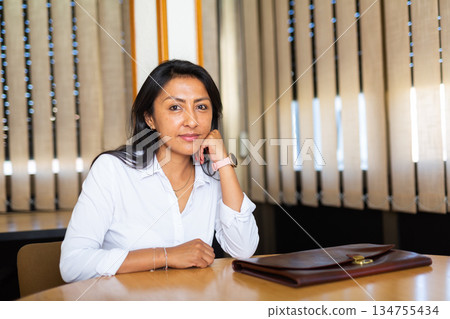 Satisfied businesswoman at the negotiation table in office Satisfied businesswoman at the negotiation table in office 134755434