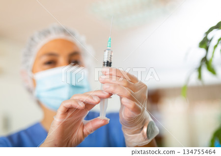 Female nurse in mask holding syringe for injection Female nurse in mask holding syringe for injection 134755464