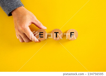 Hand arranging wooden blocks forming etf on yellow surface 134756595
