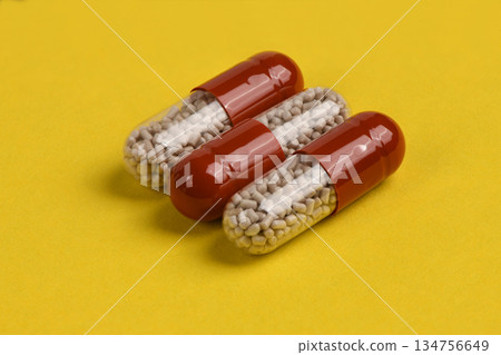 Three Red Medicine Capsules in a Row on Yellow Background Three Red Medicine Capsules in a Row on Yellow Background 134756649