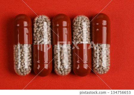 Row of Red and Clear Medical Capsules Filled with Pellets on Red Background Row of Red and Clear Medical Capsules Filled with Pellets on Red Background 134756653