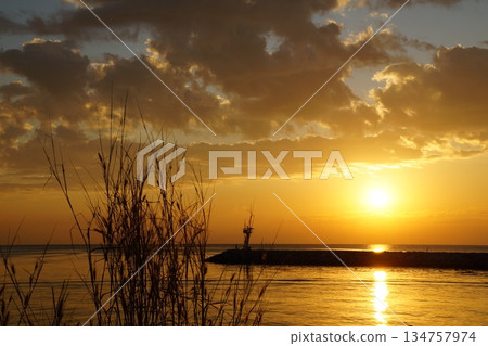 A large, bright, golden sun rises from the horizon against a backdrop of a stone pier, large rocks, A large, bright, golden sun rises from the horizon against a backdrop of a stone pier, large rocks, 134757974
