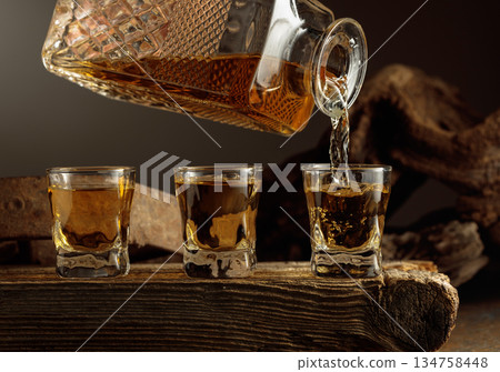 Whiskey is poured from a decanter into a shots. 134758448
