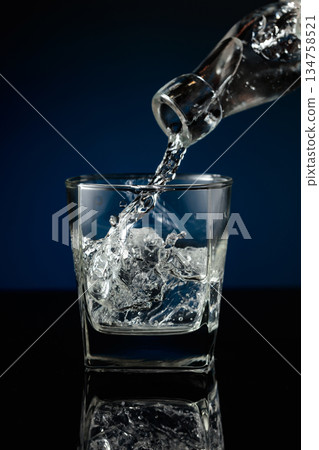 Crystal clear vodka being poured over ice in a glass. Crystal clear vodka being poured over ice in a glass. 134758521