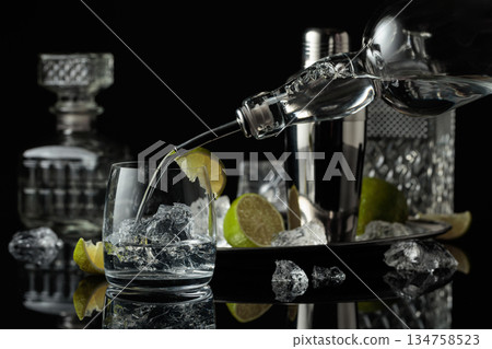Vodka is poured into a glass with ice. Vodka is poured into a glass with ice. 134758523