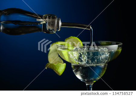 Vodka or gin is poured into a glass with ice. Vodka or gin is poured into a glass with ice. 134758527