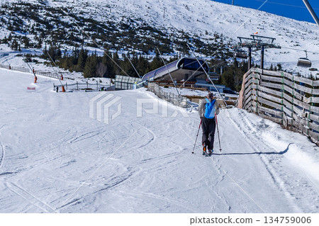 Skier with backpack walking towards a ski lift station in the mountains. Skier with backpack walking towards a ski lift station in the mountains. 134759006