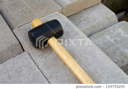 Rubber mallet with a wooden handle lying on grey concrete paving blocks. Construction and paving work concept 134759205