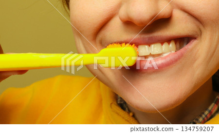 Close-up of a smiling person brushing their teeth with a bright yellow toothbrush. Concept of oral hygiene, dental care, and morning routine 134759207