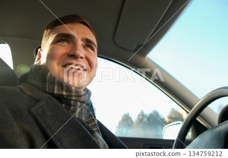 Smiling young man wearing a coat and scarf sitting in the driver seat of a car. Lifestyle and travel concept Smiling young man wearing a coat and scarf sitting in the driver seat of a car. Lifestyle and travel concept 134759212