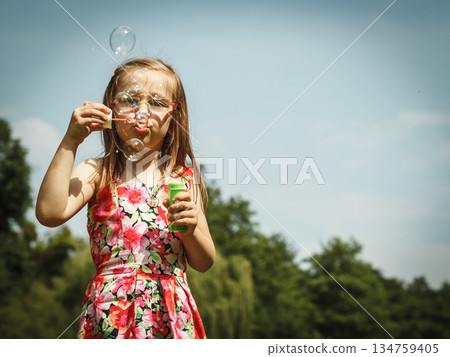 Little girl having fun blowing soap bubbles in park. 134759405