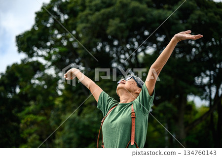An elderly woman spreads her arms outdoors. 134760143