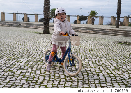 Little girl riding a two wheeled bicycle wearing a helmet 134760799