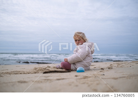 Little girl playing on a beach in cold autumn weather 134760805