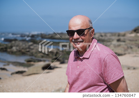 An elderly man with a mustache walking on the beach, enjoying his vacation. 134760847