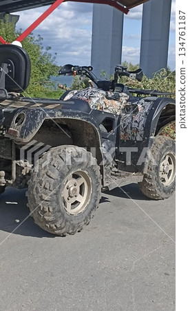 A rugged camouflage all-terrain vehicle (ATV) is covered in mud, indicating recent off-road use. Ideal for outdoor adventures, nature exploration, and recreational activities. 134761187