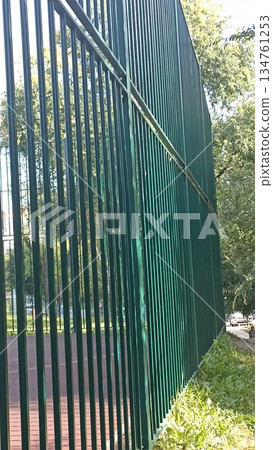 A green metal fence encloses an outdoor court, emphasizing themes of security and recreation, perfect for illustrating safety, sports, and community engagement in visuals. 134761253