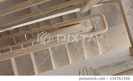 A unique perspective of a modern staircase shaft. The architectural design forms an intriguing geometric pattern, suitable for backgrounds that emphasize depth and descent. A unique perspective of a modern staircase shaft. The architectural design forms an intriguing geometric pattern, suitable for backgrounds that emphasize depth and descent. 134761398