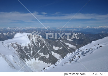 A stunning rock formation covered in snow, set against a clear blue sky with fluffy clouds in the background, creating a peaceful and breathtaking mountain landscape. 134761513