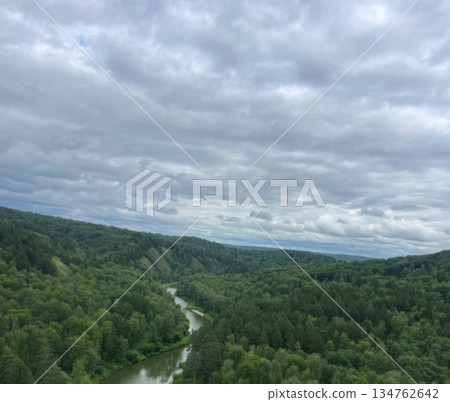 A stunning view of a lush valley with a winding river through a dense forest under a cloudy sky. Ideal for travel brochures or nature blogs, showcasing the beauty of the great outdoors. 134762642